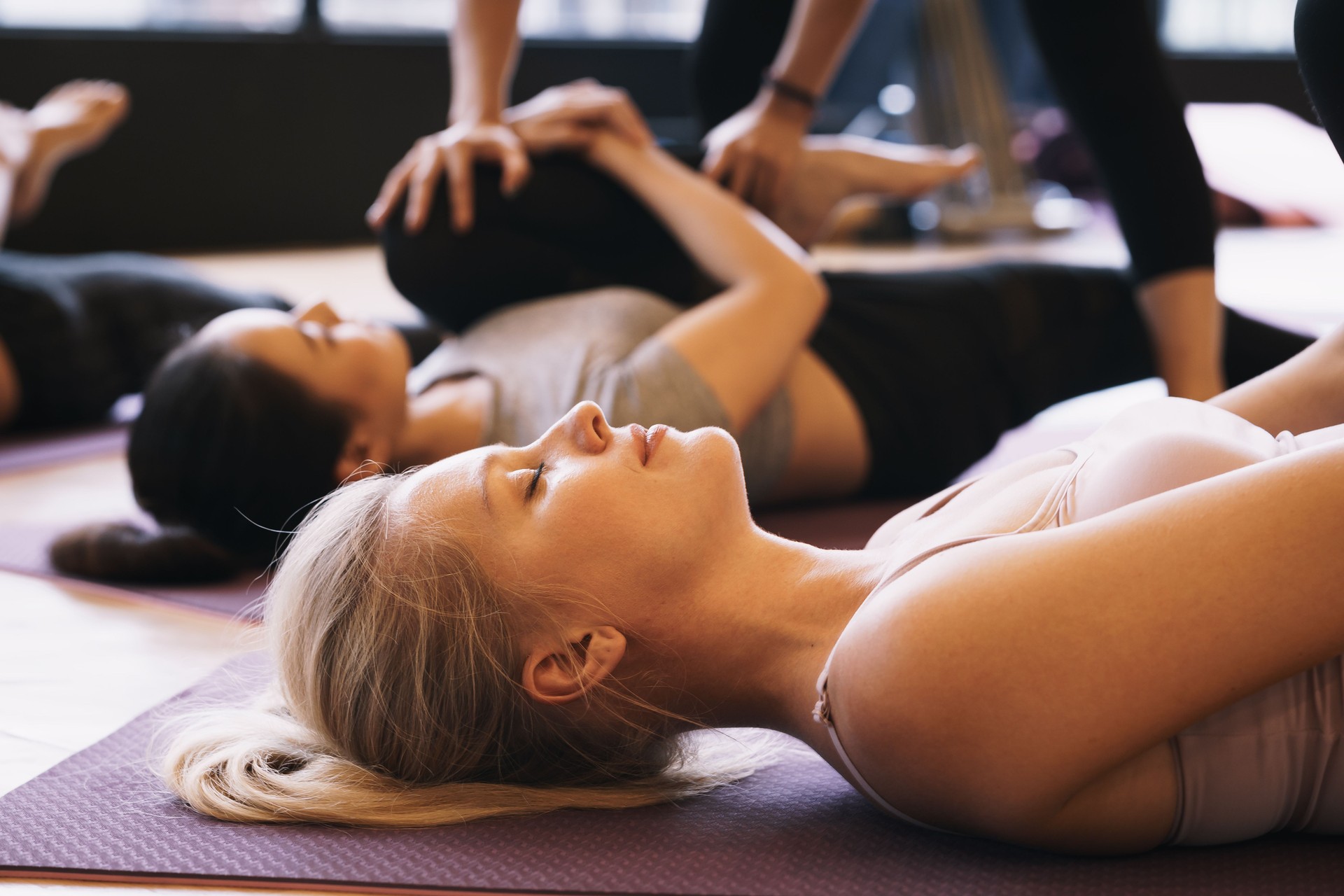 Group of young people in practicing yoga lying  pose on yoga mats with trainer in a gym, Concept of relaxation and meditation