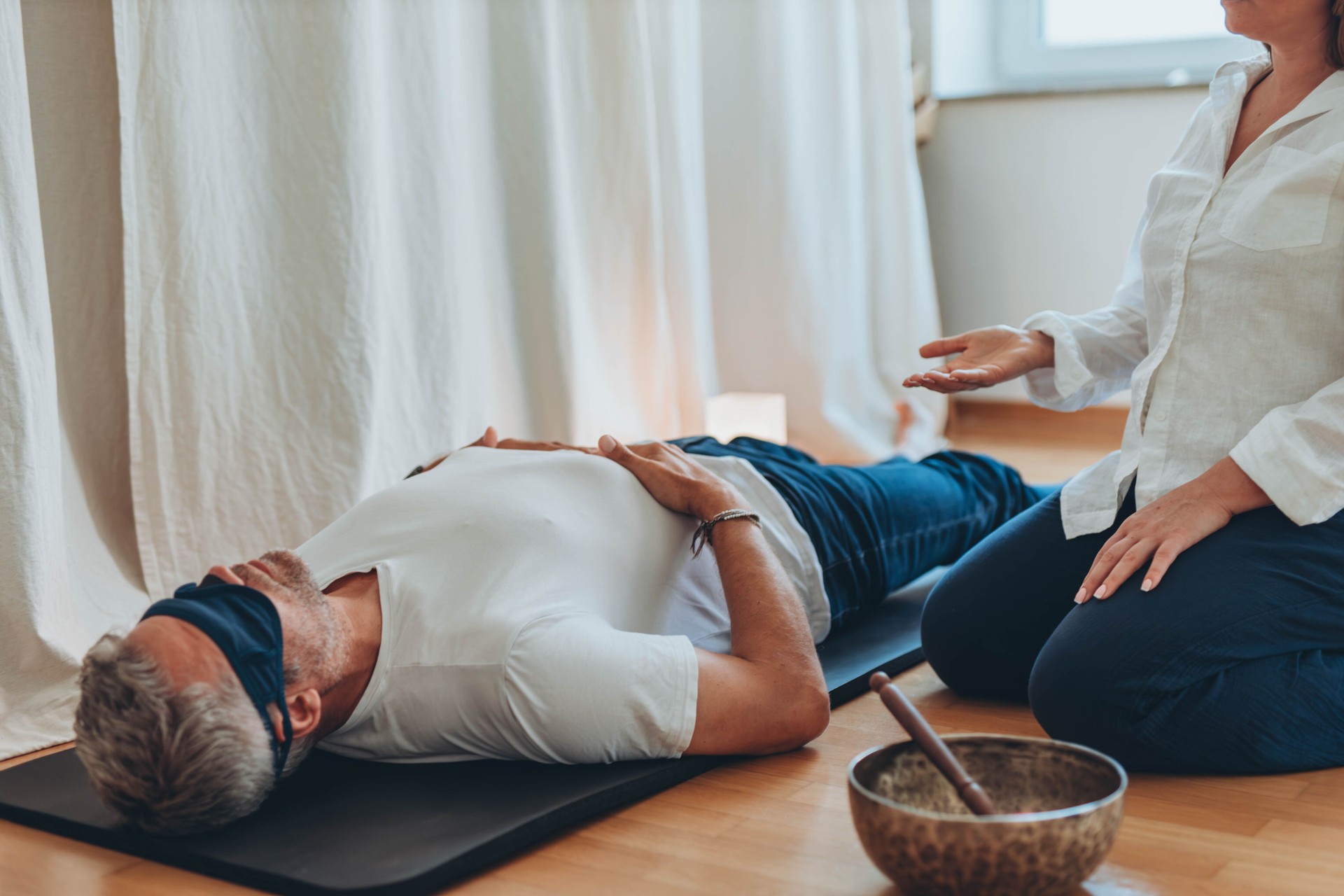 Man and woman practicing mindful breathing together during a meditation session,seated on mats with sound bowls